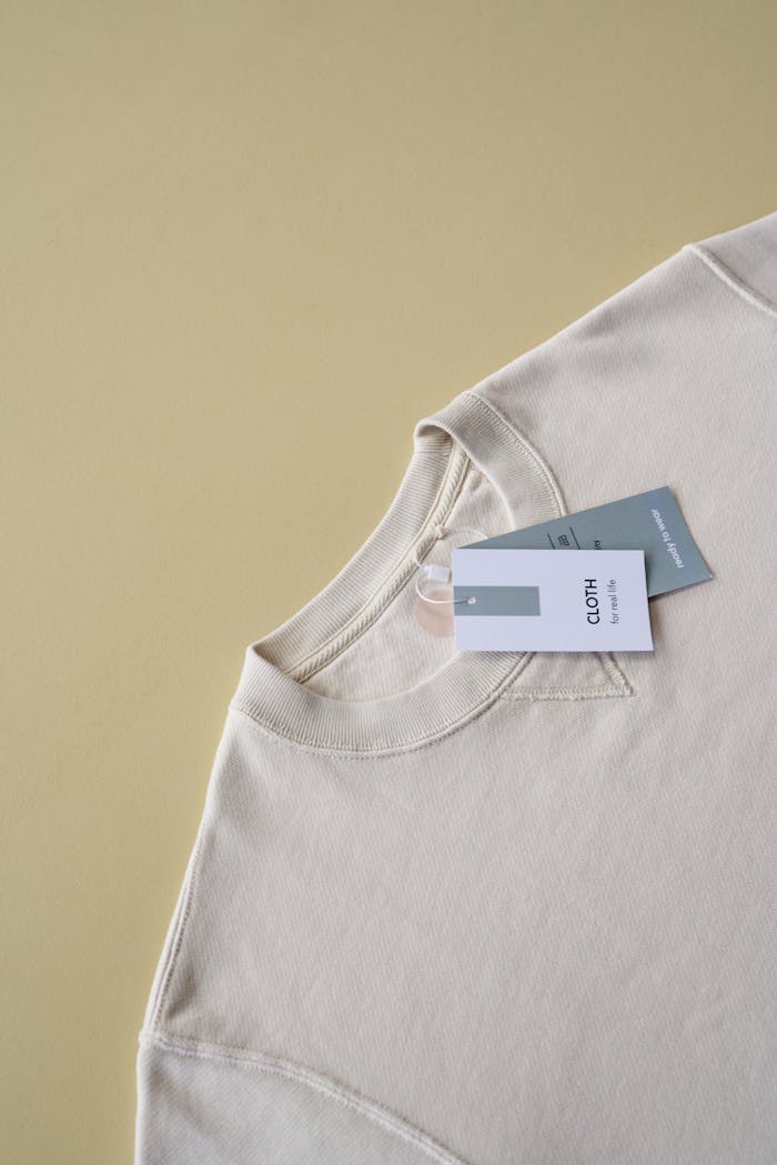 Neutral toned sweatshirt with clothing tags on soft beige background, ideal for fashion branding.